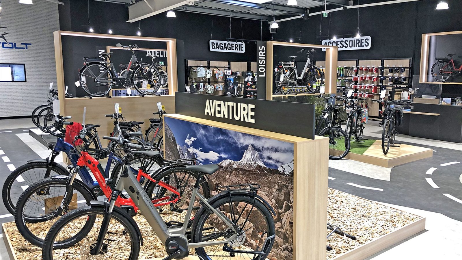 L'intérieur d'un magasin de vélos moderne présente divers vélos, accessoires et équipements sur des racks et des étagères, avec des panneaux en français indiquant les différentes sections.