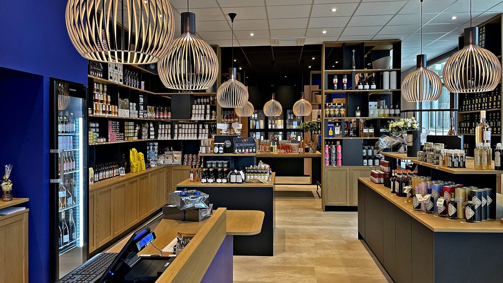 Intérieur d'une épicerie fine moderne avec des étagères en bois, des lampes suspendues et divers produits emballés présentés dans l'espace.