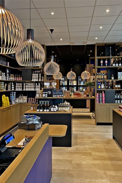 Intérieur d'une épicerie fine moderne avec des étagères en bois et des lampes suspendues, présentant divers aliments emballés, des bocaux et des bouteilles soigneusement disposés dans le magasin.