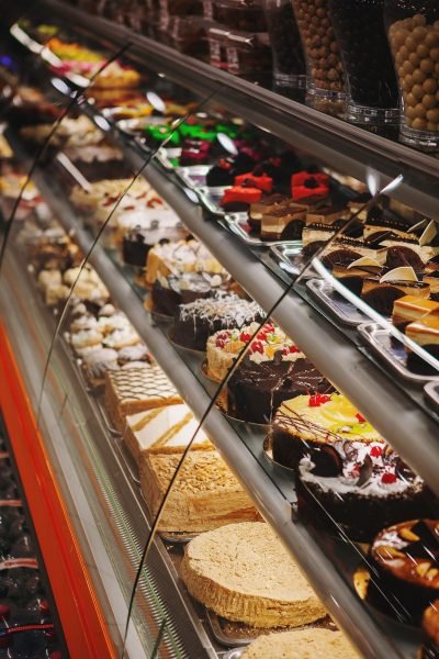 Une vitrine remplie d'un assortiment de gâteaux, de pâtisseries et de desserts disposés en rangées met en valeur l'agencement boulangerie expert que l'on trouve dans les meilleures boulangeries ou pâtisseries.