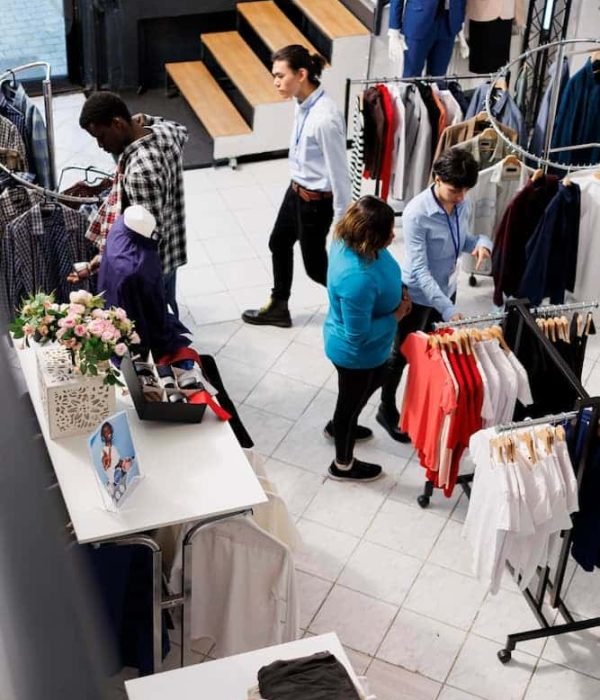 Des personnes font du shopping et interagissent avec le personnel à l'intérieur d'un magasin de vêtements, avec des étagères de vêtements et des mannequins en exposition.